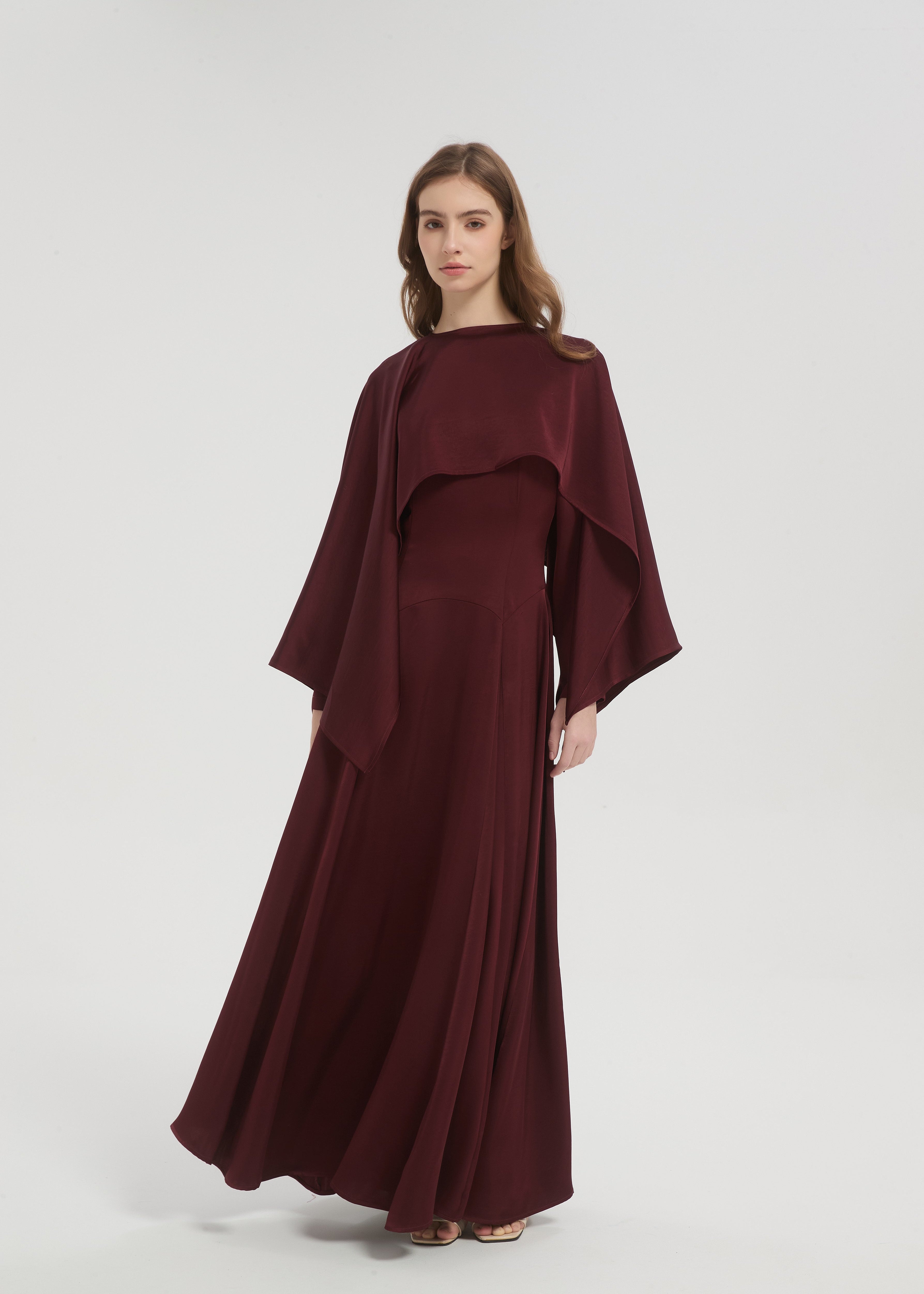 Woman wearing a burgundy dress with cape on a white background